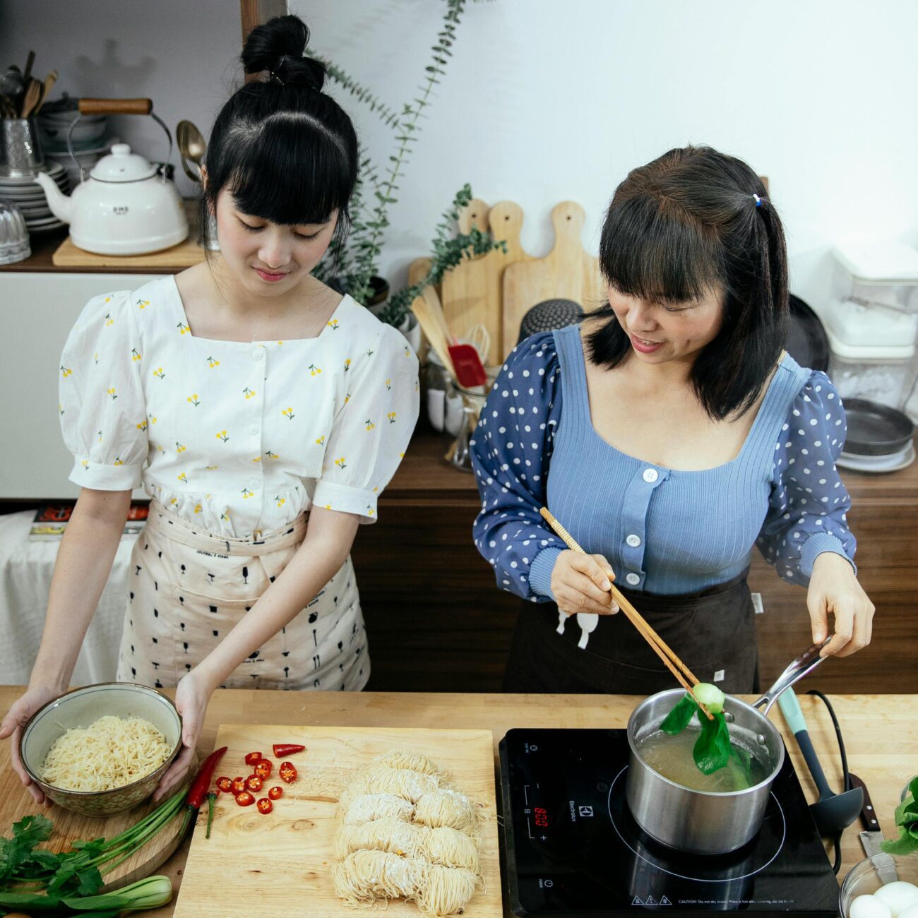 From above content Asian female adding boiled pak choi cabbage into bowl with homemade noodle while cooking traditional yummy Asian soup